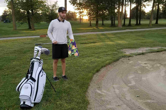man beside golf bunker wiping golf clubhead 