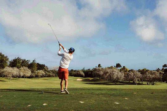 man wearing white shirt hitting golf iron completing his backswing 